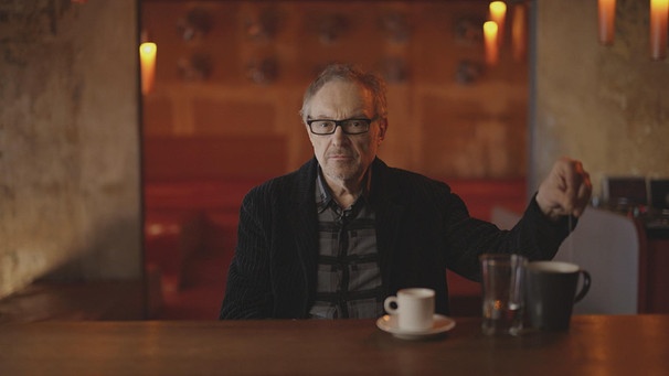 Ein Mann mit Brille sitzt vor der Kamera, vor ihm ein Holztisch, auf welchem mehrere Tassen stehen.  | Bild: BR
